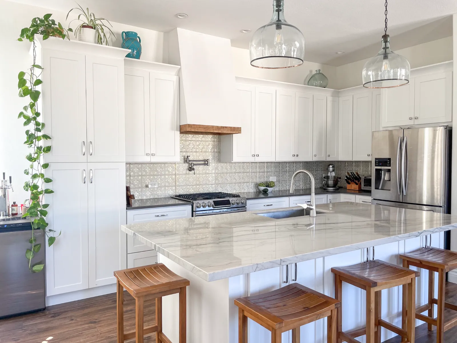 Bright kitchen with white shaker cabinetry, a marble island with wood stools, patterned tile backsplash, and glass pendant lights.